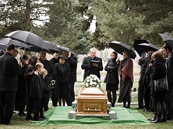 Image of a funeral in the rain with family holding umbrellas over the casket. Avoid frozen bank accounts after death