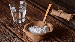 Baking soda in a wood bowl with a wooden spoon, next to a glass of water indicating the health benefits of baking soda