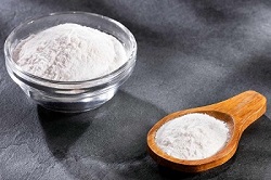 Baking soda in a glass bowl and a wooden spoon provide baking soda health benefits